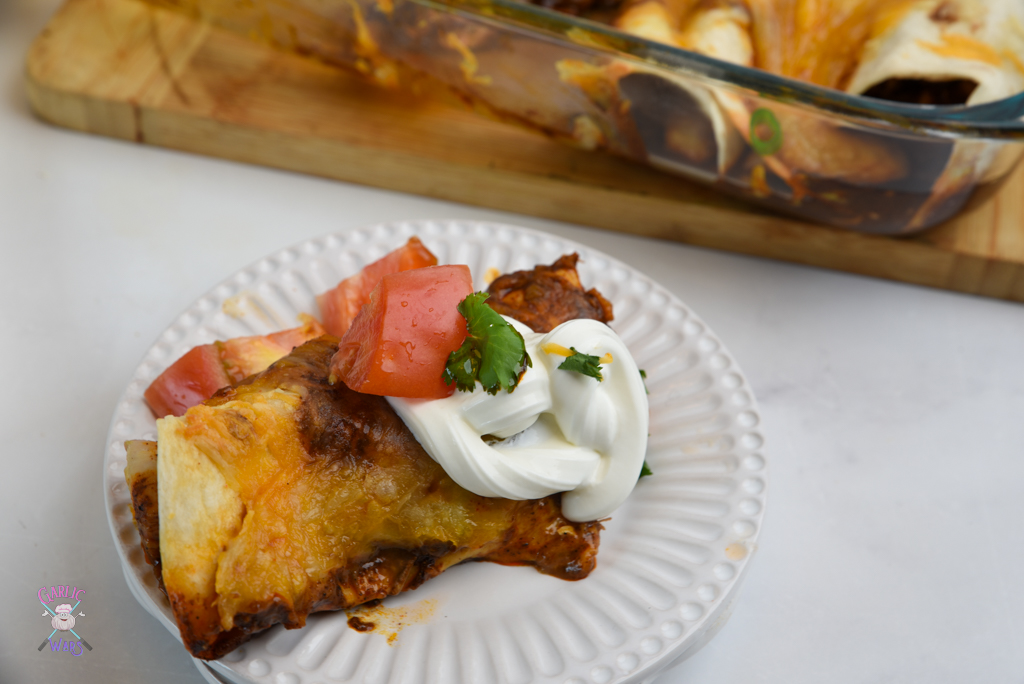 chicken enchilada on small white plate, topped with sour cream and tomatoes