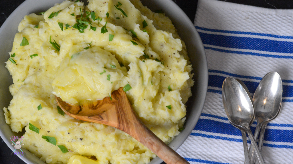 A large grey bowl of mashed potatoes, with a bit of potato on a wooden spoon.