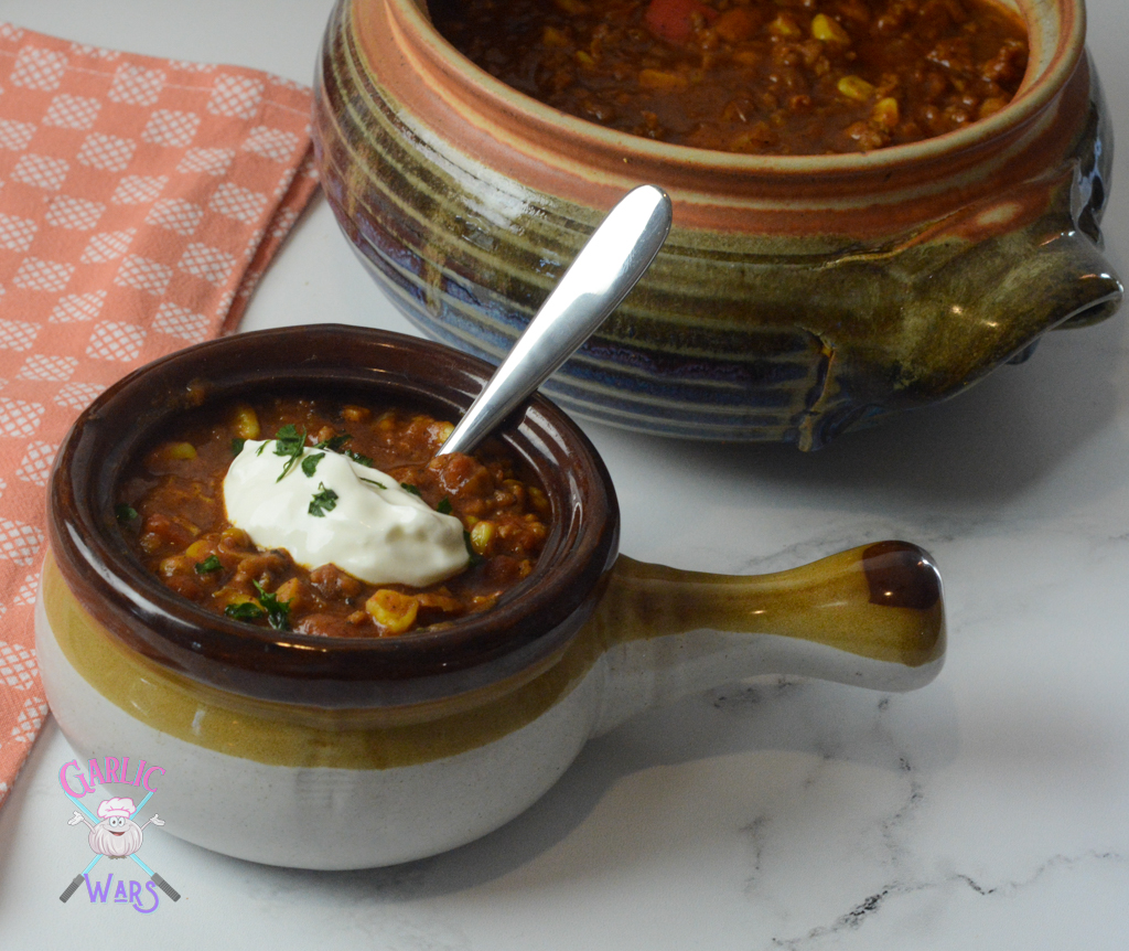 small bowl of pumpkin chili topped with sour cream, in front of large pot of chili