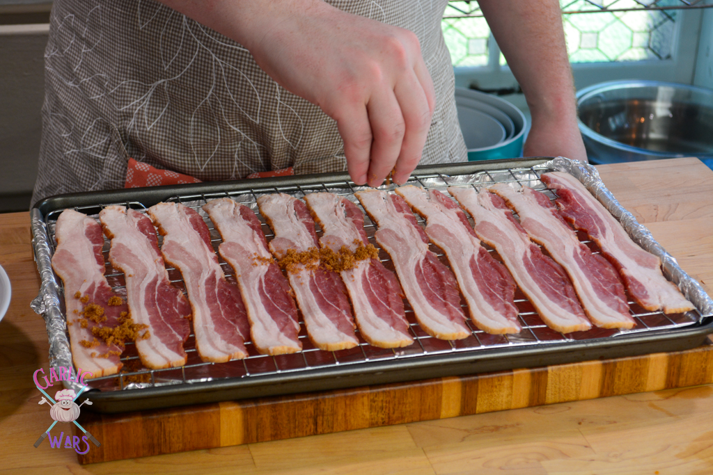 Uncooked bacon on wire rack, being sprinkled with brown sugar.