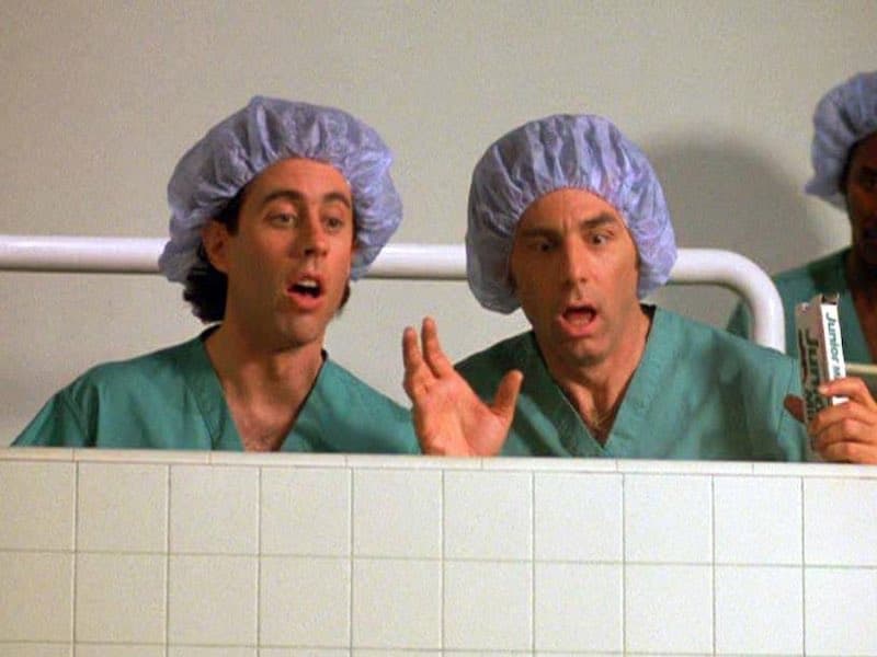 Jerry and Kramer in scrubs and hairnets, watching a Junior Mint fall into an open surgery.