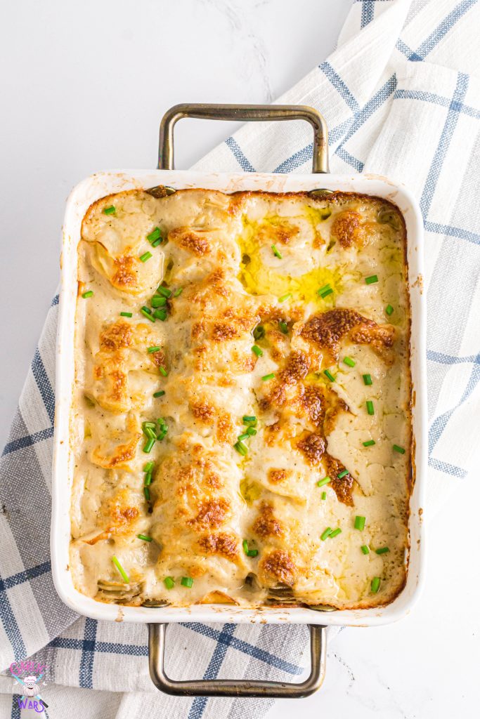 scalloped potatoes in a white casserole dish on top of a blue plaid linen